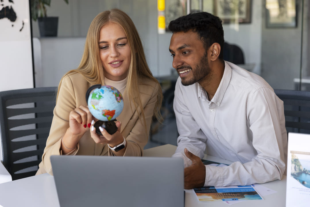 Uma mulher e um homem conversando com um globo terrestre na mão, como se estivessem interessados na carreira de negócios internacionais.